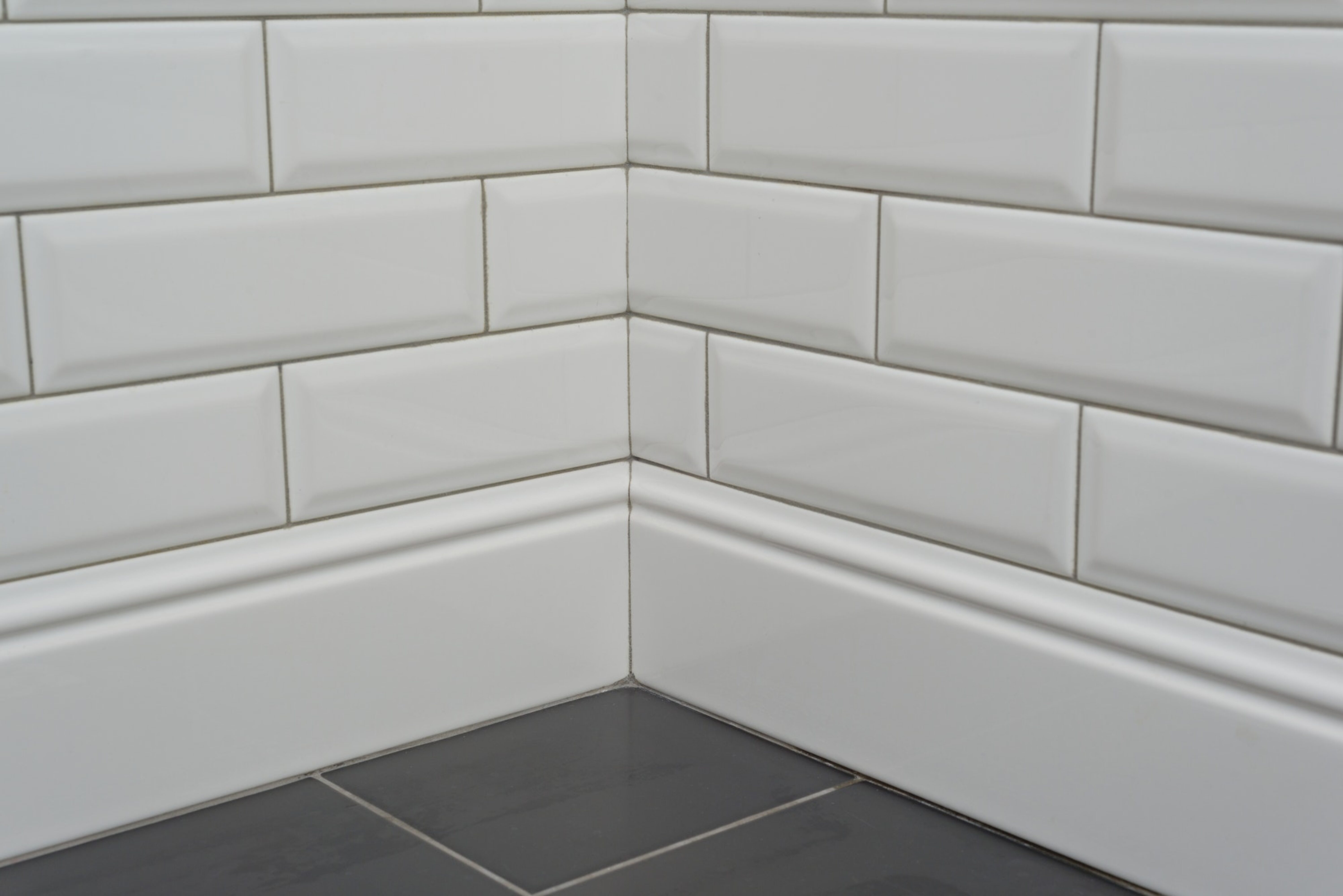 Close-up corner covered with white decorative tiles with high ceramic plinth, molding, curb, and