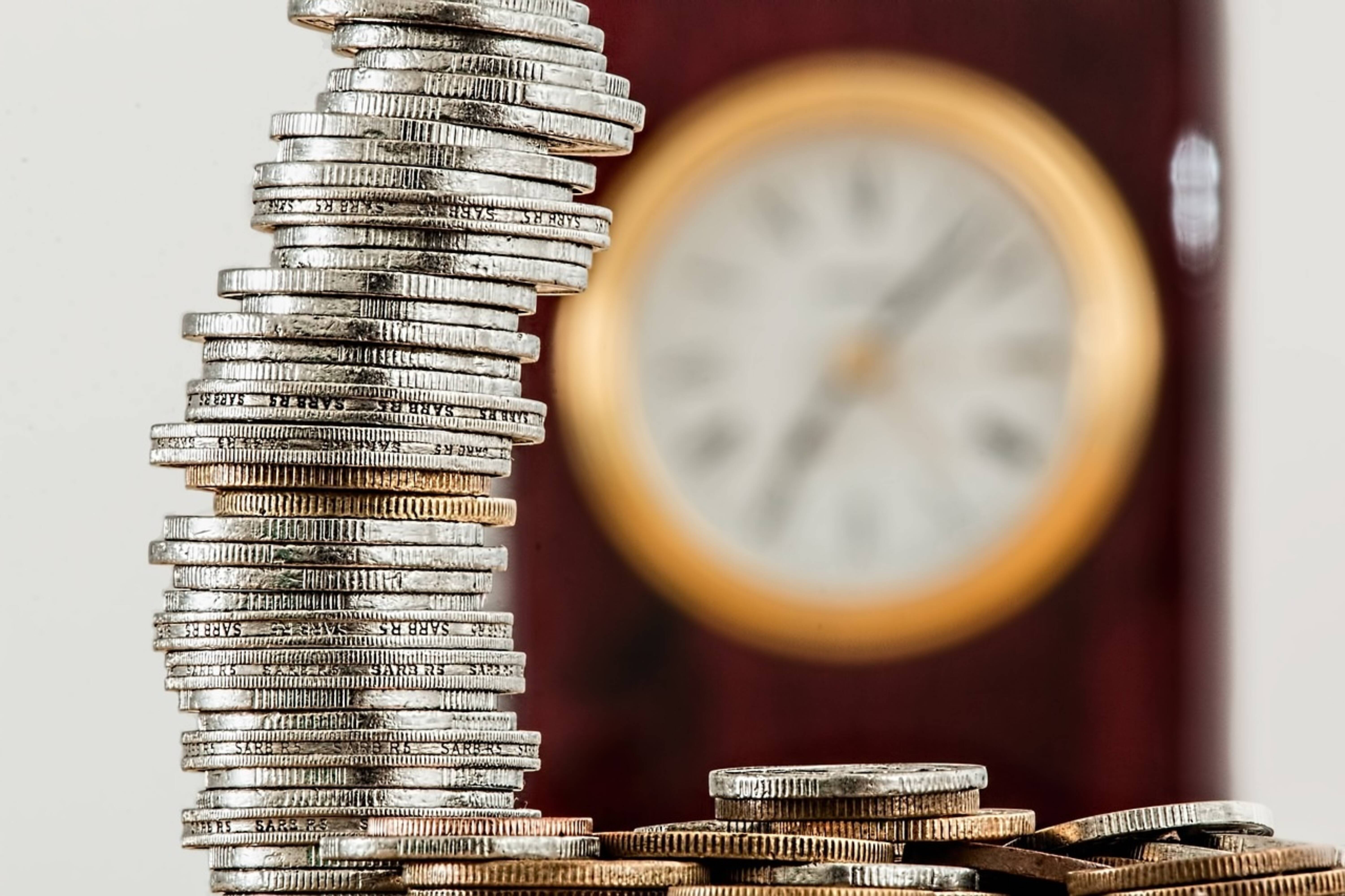 A stack of silver coins before a clock.