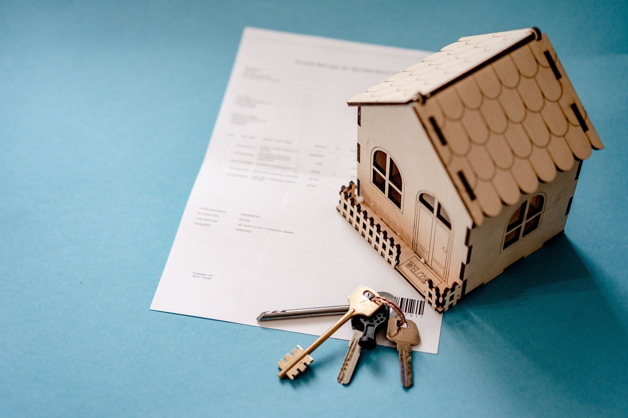 A miniature house and keys next to a contract.