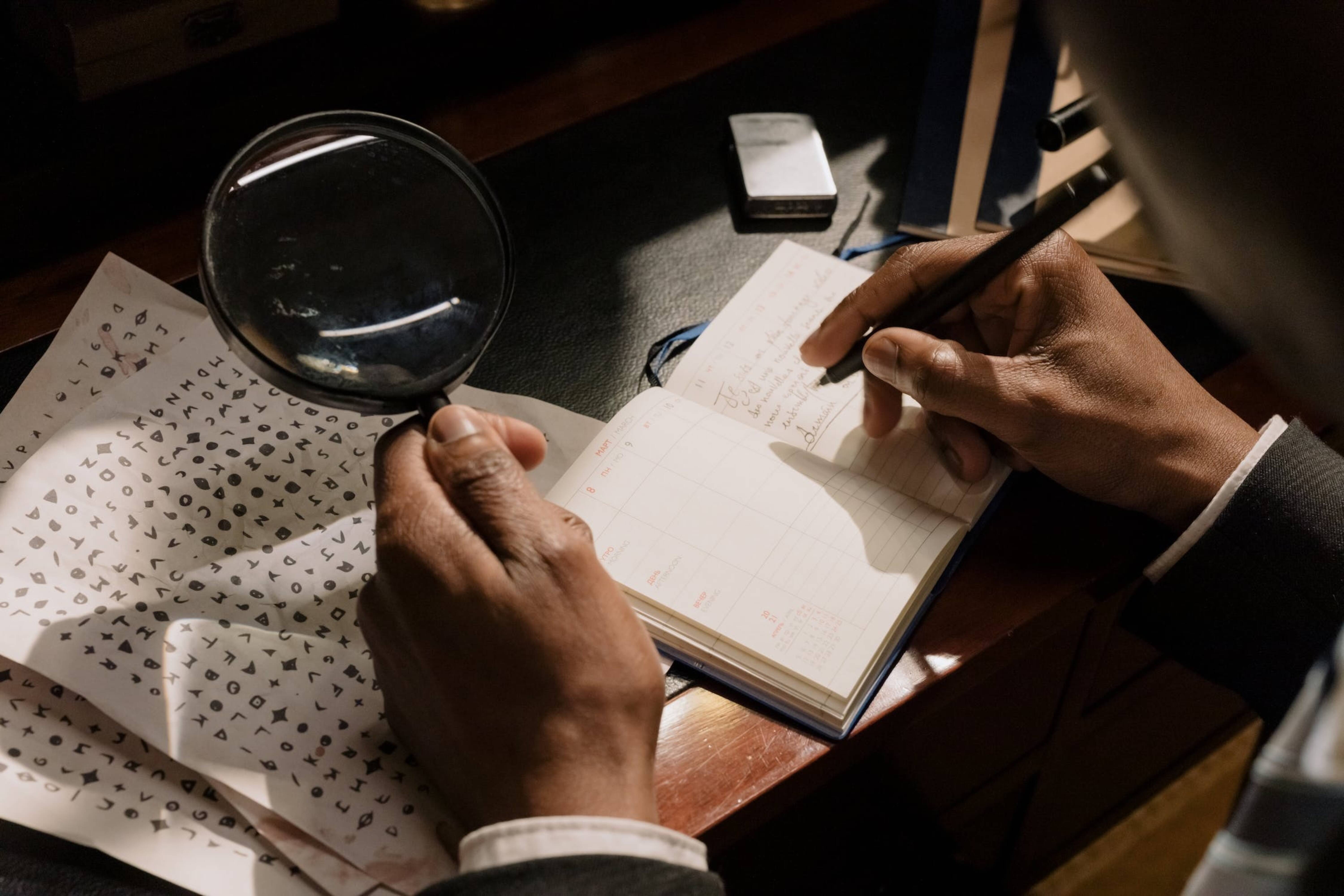 A man holding a magnifying glass and keeping notes.