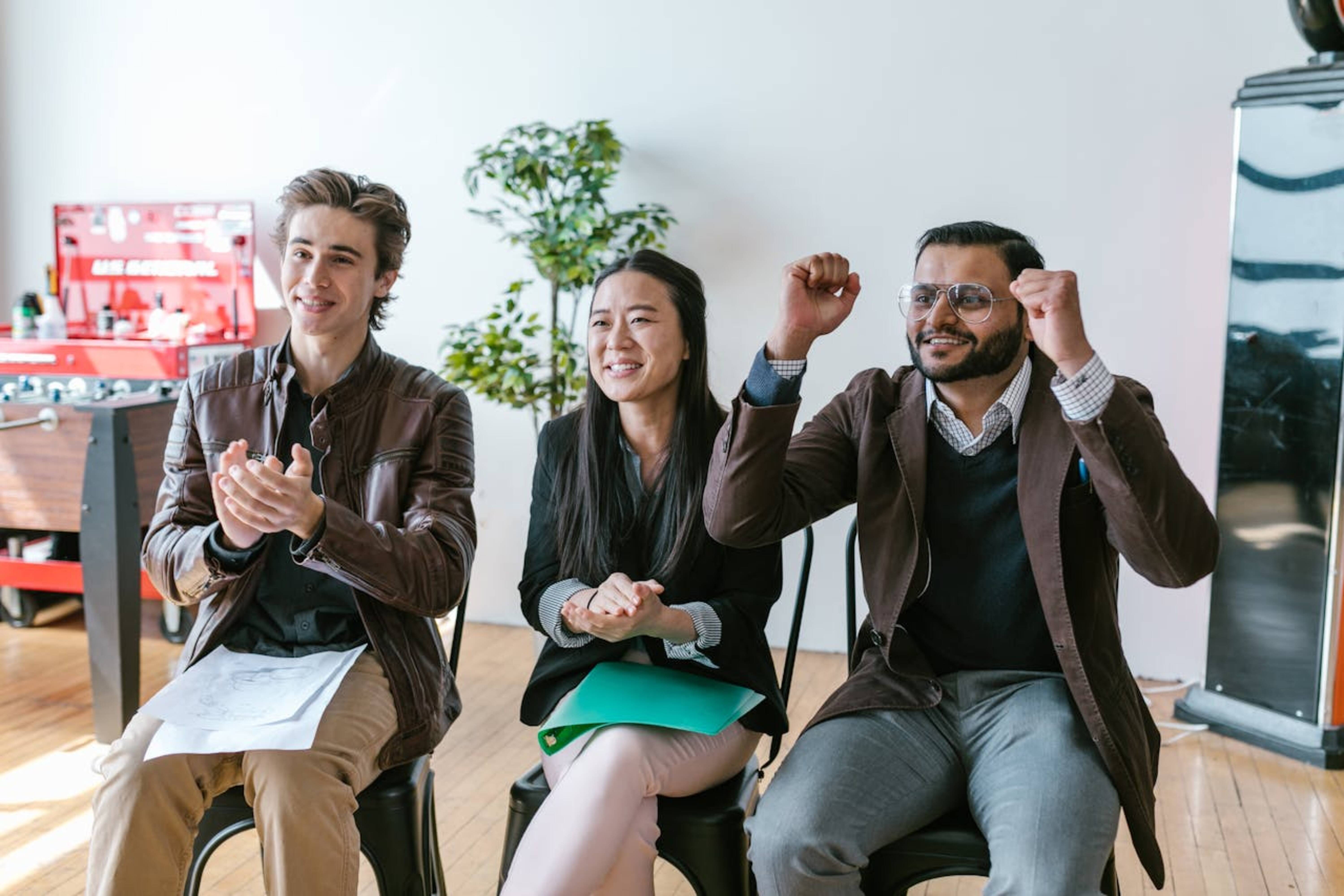 Three happy people clapping in the office.
